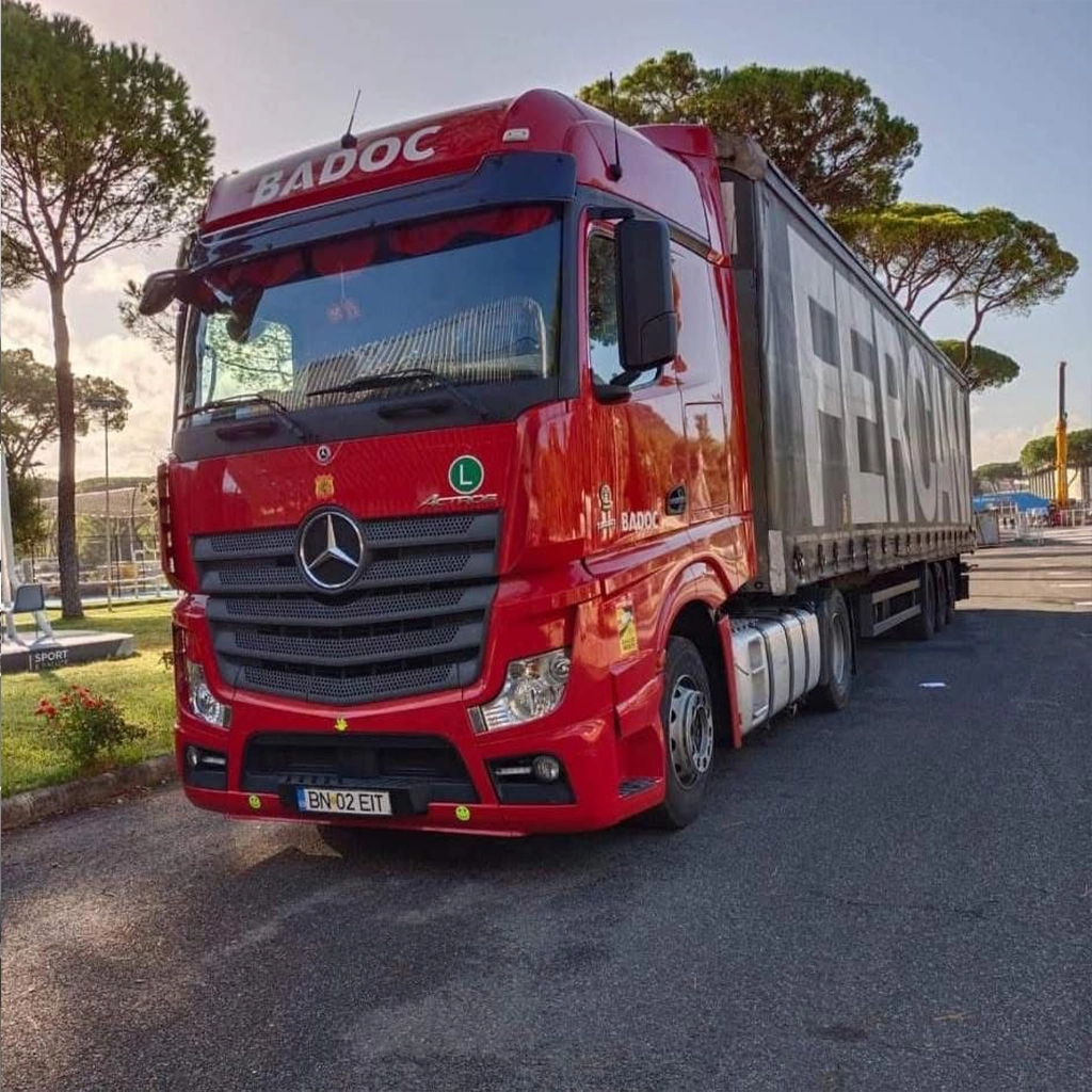 Camion Mercedes-Benz rosu si semiremorca cu prelata fotografiate in parcare